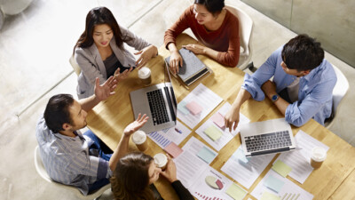 Executives sitting around a table, spread with laptops and paperwork.