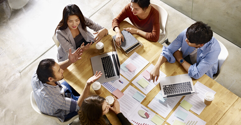 Executives sitting around a table, spread with laptops and paperwork.