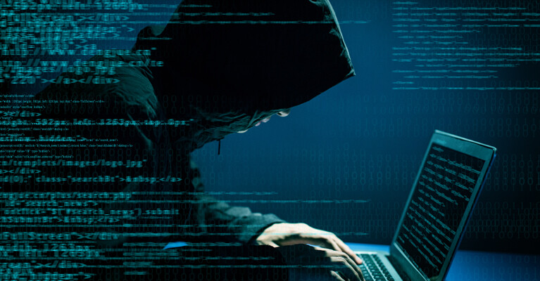 A man in a hood hacking into a computer.