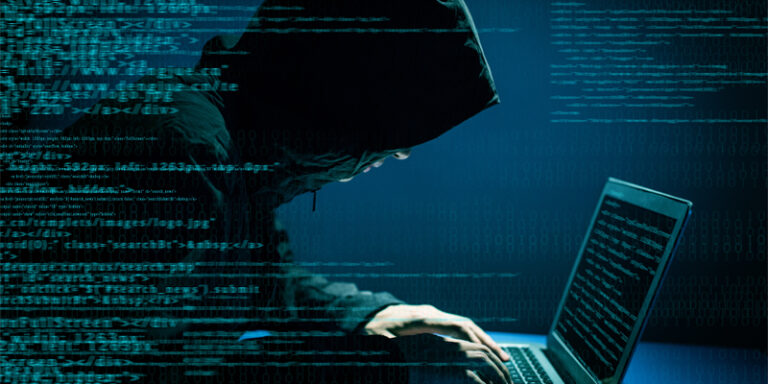 A man in a hood hacking into a computer.