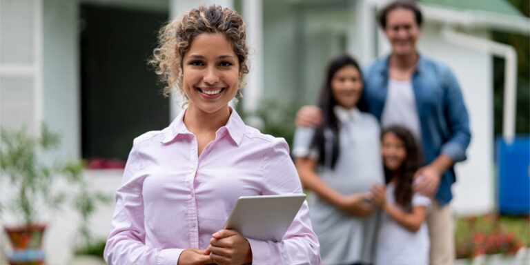 Real estate agent holding tablet, smiling with a family in front of a house.