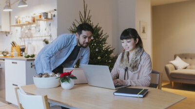 A man and a woman using a laptop inside an apartment, decorated for Christmas.