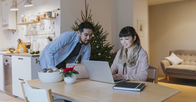 A man and a woman using a laptop inside an apartment, decorated for Christmas.