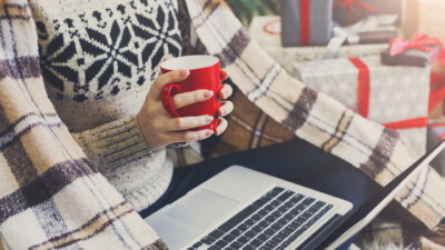 A person holding a coffee mug while shopping online for the holidays.