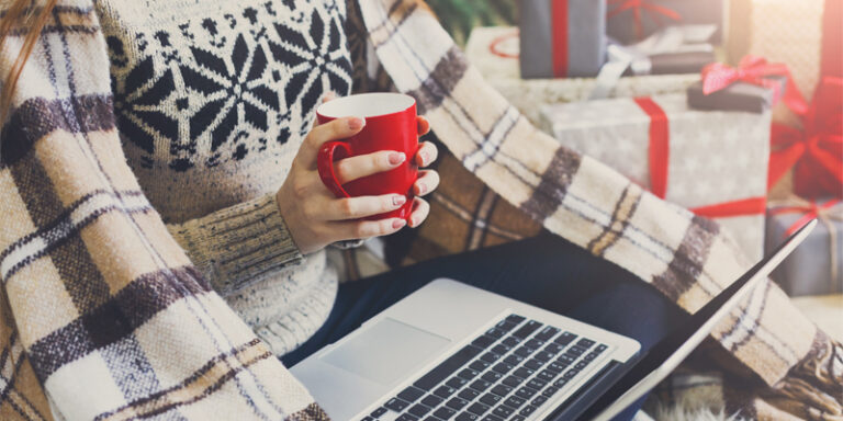A person holding a coffee mug while shopping online for the holidays.