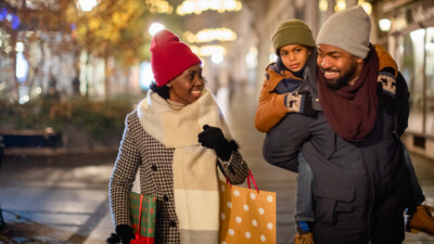 Woman, man, and child walking down the street with shopping bags.