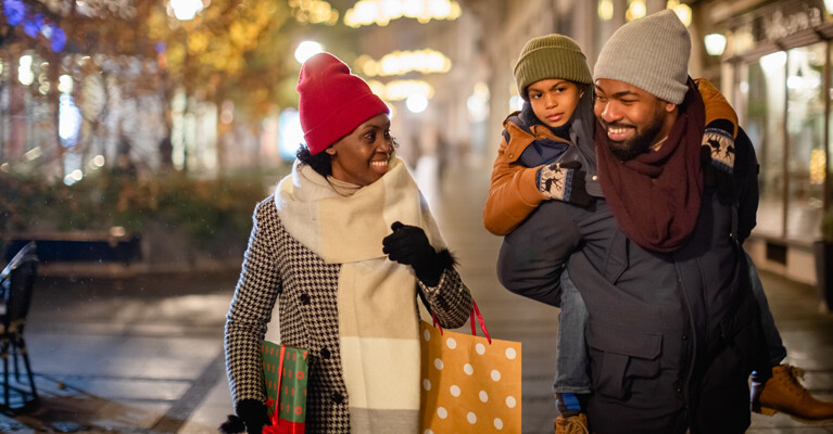 Woman, man, and child walking down the street with shopping bags.