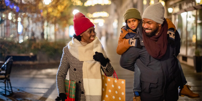 Woman, man, and child walking down the street with shopping bags.