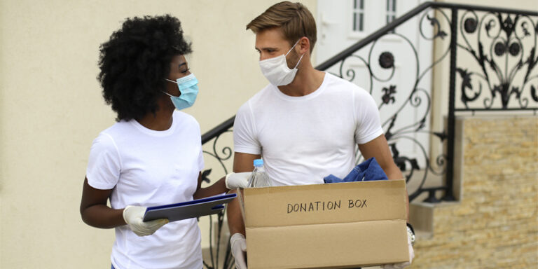 A man and a woman carrying a box of supplies to be donated to charity.