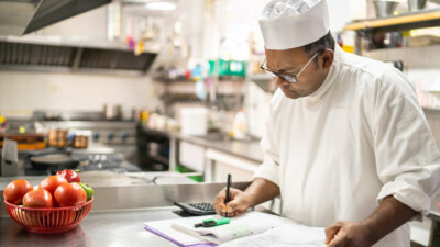 A chef writing in a notebook and using a calculator.