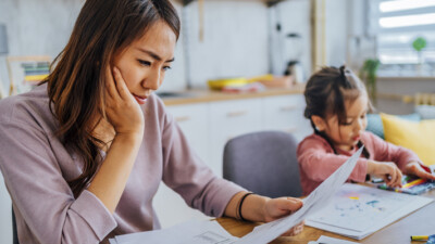 A mother reviewing her finances while her child plays in the background.