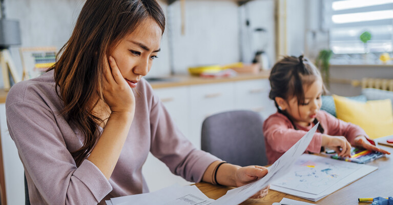 A mother reviewing her finances while her child plays in the background.