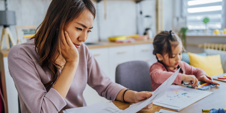 A mother reviewing her finances while her child plays in the background.