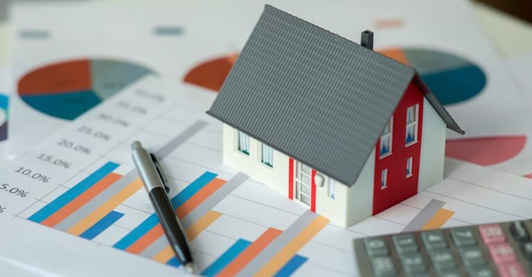 Model home on top of papers showing charts.