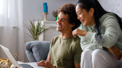 A couple laughing in front of their computer.