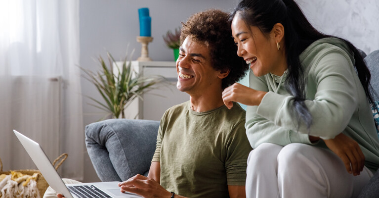 A couple laughing in front of their computer.