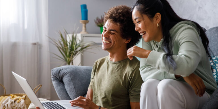 A couple laughing in front of their computer.