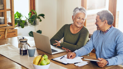 A man and a woman using their laptop at the kitchen table.