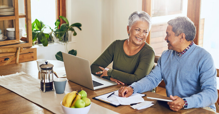 A man and a woman using their laptop at the kitchen table.