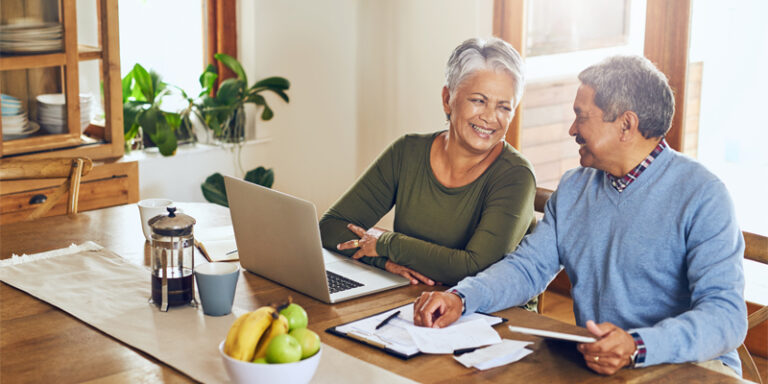 A man and a woman using their laptop at the kitchen table.