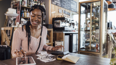 A business owner calculating their business finances using a calculator and a tablet.