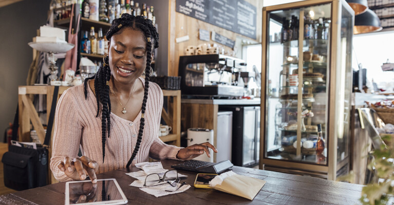 A business owner calculating their business finances using a calculator and a tablet.