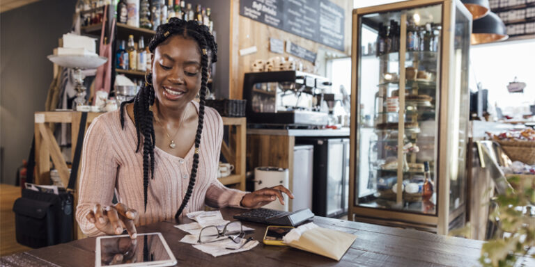 A business owner calculating their business finances using a calculator and a tablet.