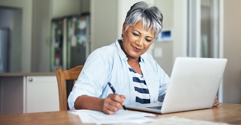 Woman using laptop and completing paperwork.