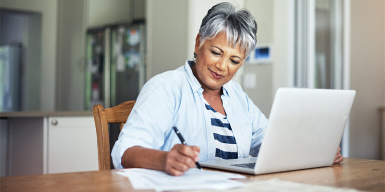 Woman using laptop and completing paperwork.
