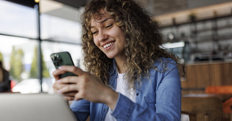 Woman smiling and looking at a cell phone.
