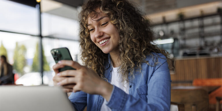 Woman smiling and looking at a cell phone.