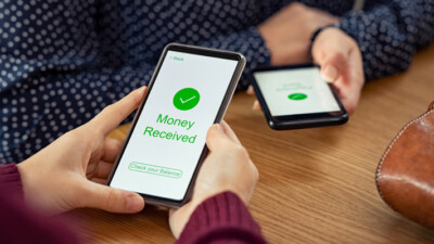 Two cell phones displaying an electronic money transfer, one screen reading "Money received. Check your balance."