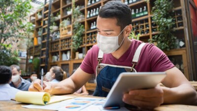 Small business owner doing paperwork and using tablet.