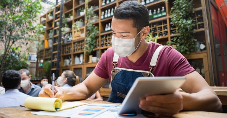 Small business owner doing paperwork and using tablet.