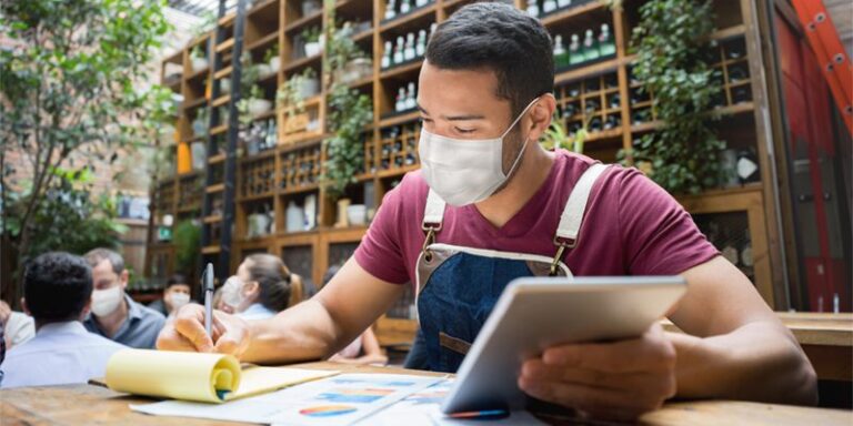 Small business owner doing paperwork and using tablet.