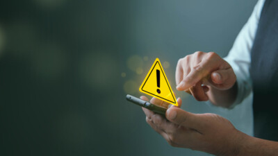 A person holding a smartphone with a warning sign above it.