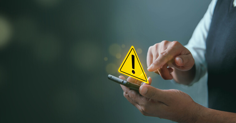 A person holding a smartphone with a warning sign above it.