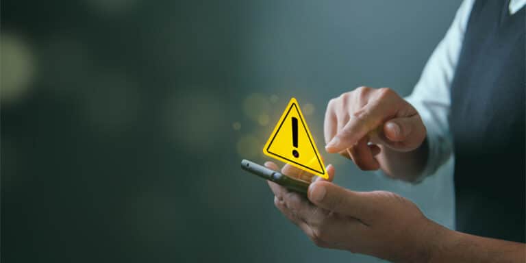 A person holding a smartphone with a warning sign above it.