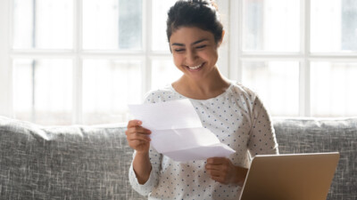 A woman smiling at a letter she is unfolding.