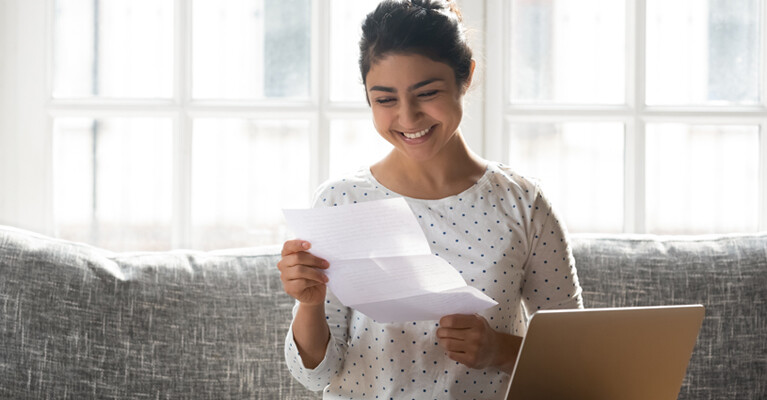 A woman smiling at a letter she is unfolding.