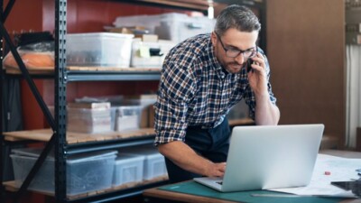 A man on the phone while looking at his laptop.