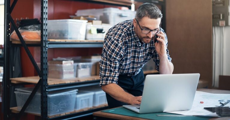 A man on the phone while looking at his laptop.