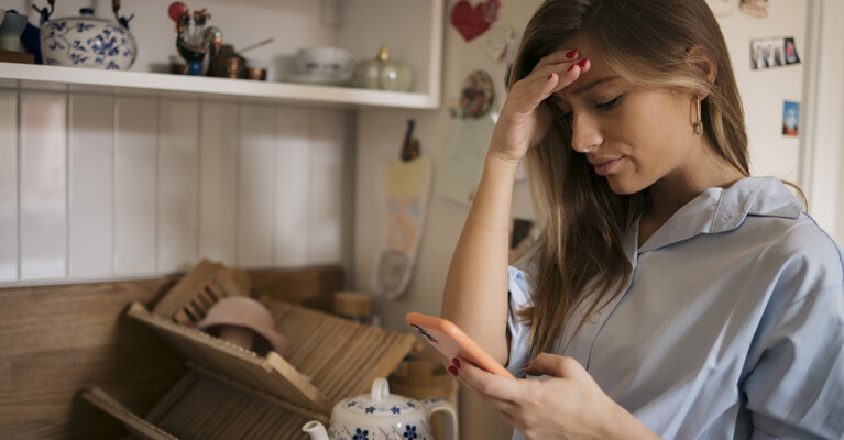 A woman looking concerned by the scam text message on her phone.