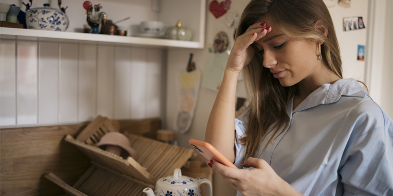 A woman looking concerned by the scam text message on her phone.