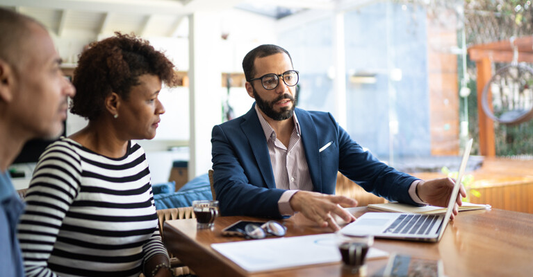 A businessman showing a man and a woman his laptop screen.