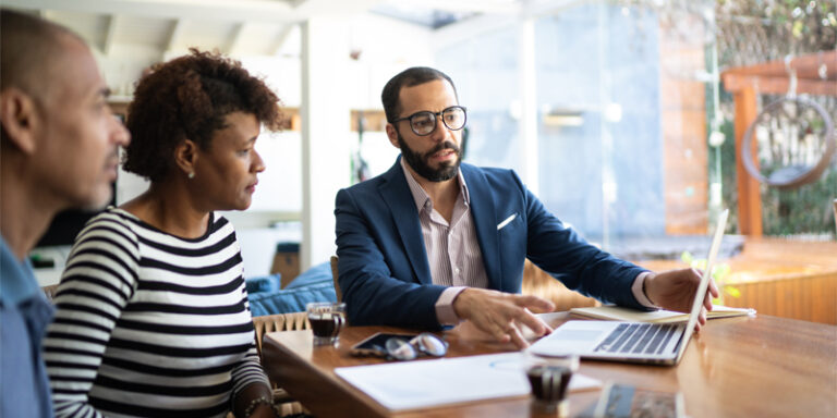 A businessman showing a man and a woman his laptop screen.