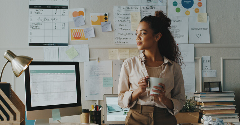 Woman holding coffee cup in front of work desk.