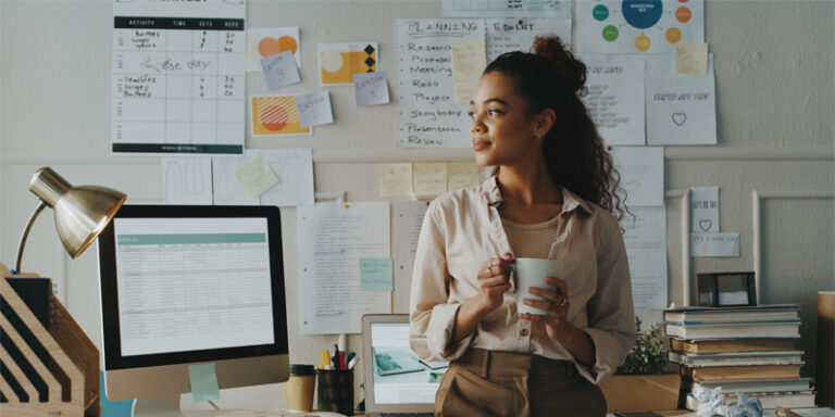 Woman holding coffee cup in front of work desk.