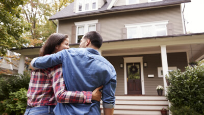 A couple embracing in front of their home.