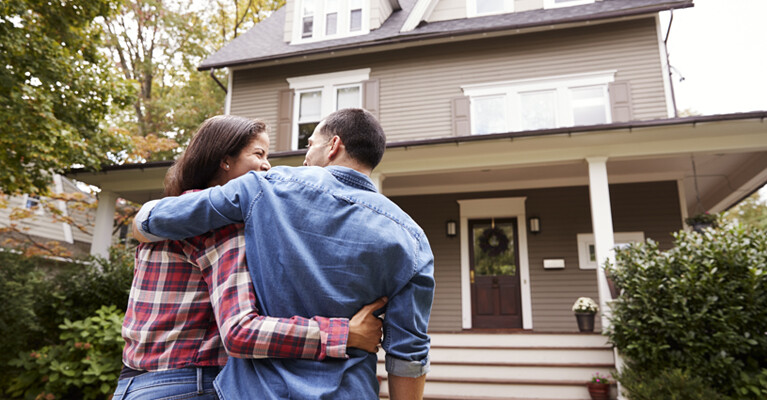 A couple embracing in front of their home.